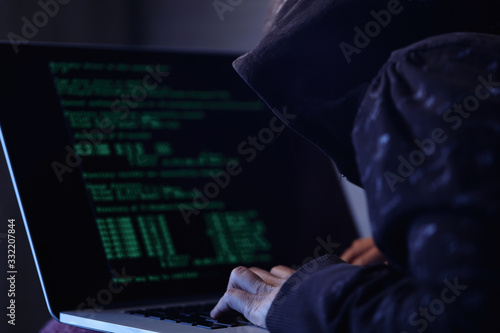 Unrecognizable computer hacker stealing data while using laptop.