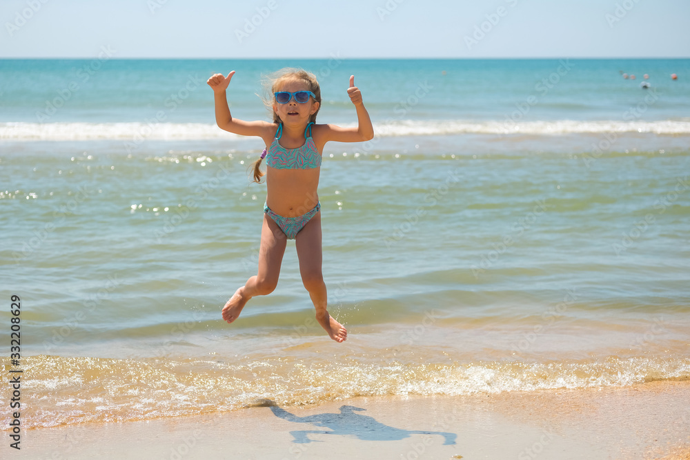 A little girl jumps on the background of the sea. A child is happy on the beach. A little girl jumps on the background of the sea. A child is happy on the beach.