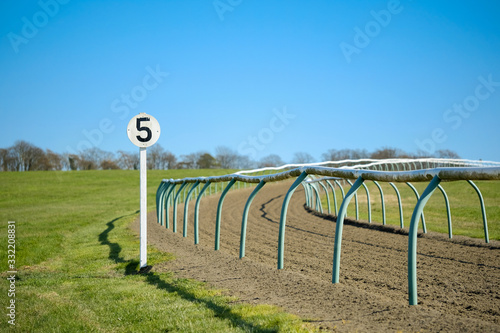 Shallow focus of a 5 furlong sign post seen at the edge of a bend at a horse rack track seen near a famous english market town. The plastic tubular fencing is visible ob both sides of track. photo