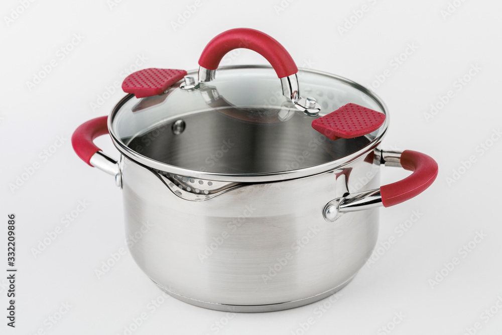 Stainless casserole with glass lid and red handles on grey background. Stainless casserole with glass lid and red handles on grey background.