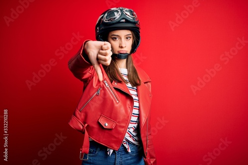 Young beautiful brunette motocyclist woman wearing motorcycle helmet and red jacket looking unhappy and angry showing rejection and negative with thumbs down gesture. Bad expression. © Krakenimages.com