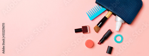 Make up products spilling out of cosmetics bag, on pink pastel background with empty space for your design