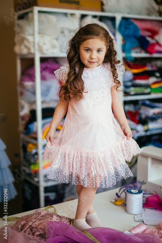 Little girl in a pink dress posing on a table in a sewing atelier