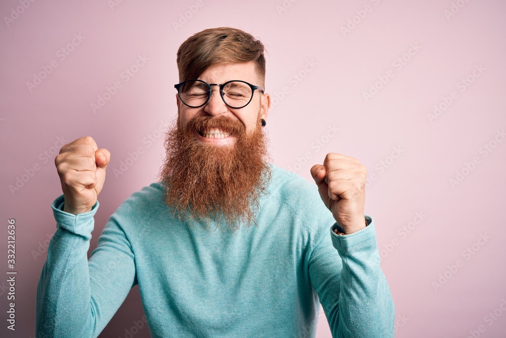Handsome Irish redhead man with beard wearing glasses over pink isolated background excited for success with arms raised and eyes closed celebrating victory smiling. Winner concept. Handsome Irish redhead man with beard wearing glasses over pink isolated background excited for success with arms raised and eyes closed celebrating victory smiling. Winner concept.