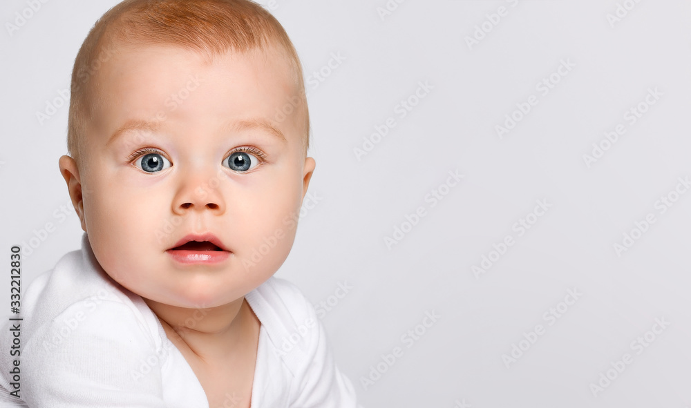 Portrait of a chubby red-haired baby in a bodysuit. He looks in surprise at the camera isolated on a white studio background.