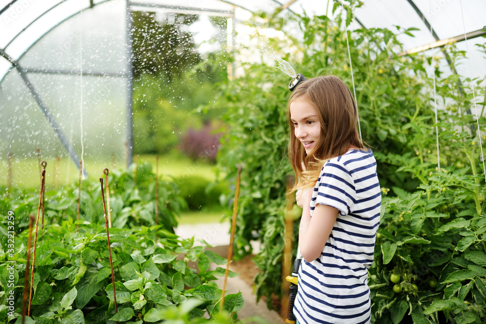 Adorable young girl watering variuos vegetables in a greenhouse on sunny summer day. Gardening activity for kids. Adorable young girl watering variuos vegetables in a greenhouse on sunny summer day. Gardening activity for kids.