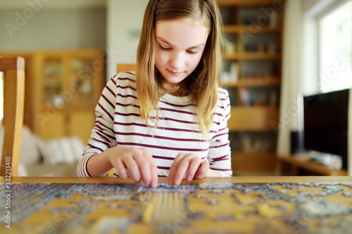 Cute young girl playing puzzles at home. Child connecting jigsaw puzzle pieces in a living room table. Kid assembling a jigsaw puzzle. Fun family leisure. photo