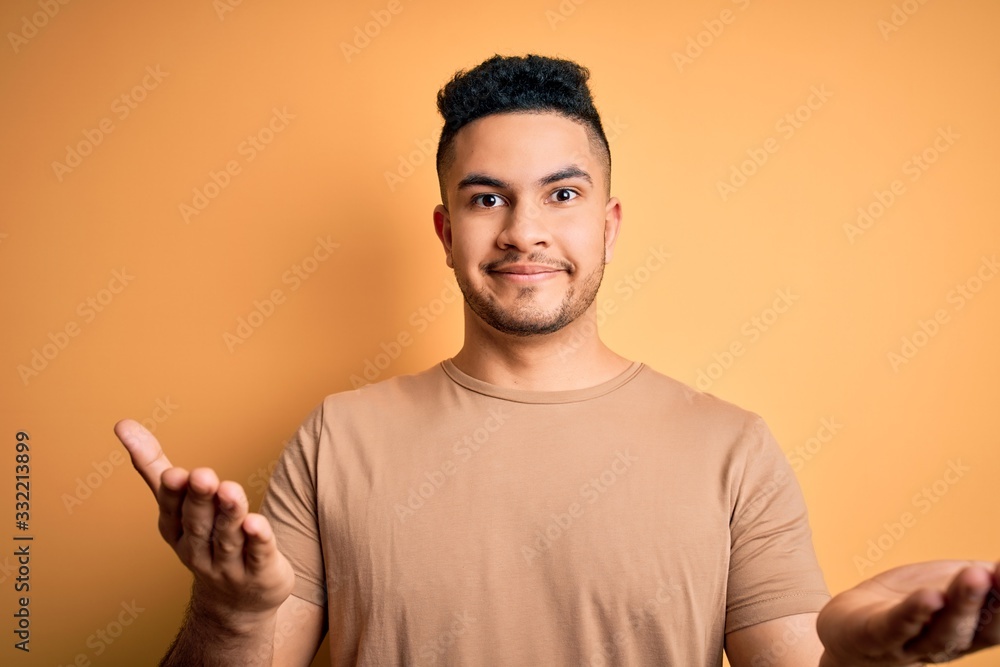 Young handsome man wearing casual t-shirt standing over isolated yellow background clueless and confused expression with arms and hands raised. Doubt concept. Young handsome man wearing casual t-shirt standing over isolated yellow background clueless and confused expression with arms and hands raised. Doubt concept.