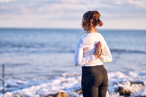 Fototapeta Naklejka Na Ścianę i Meble -  Young beautiful sportwoman practicing yoga. Coach standing on bakcview teaching reverse prayer pose at the beach