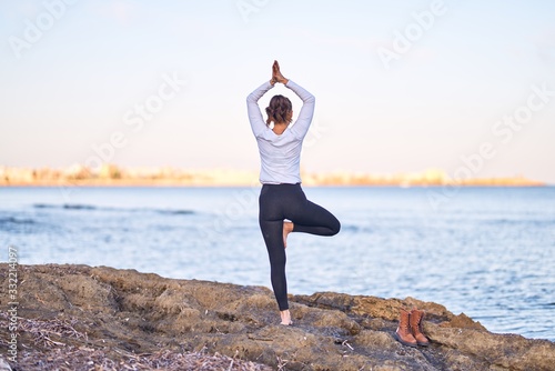 Young beautiful sportwoman practicing yoga. Coach teaching tree pose at the beach