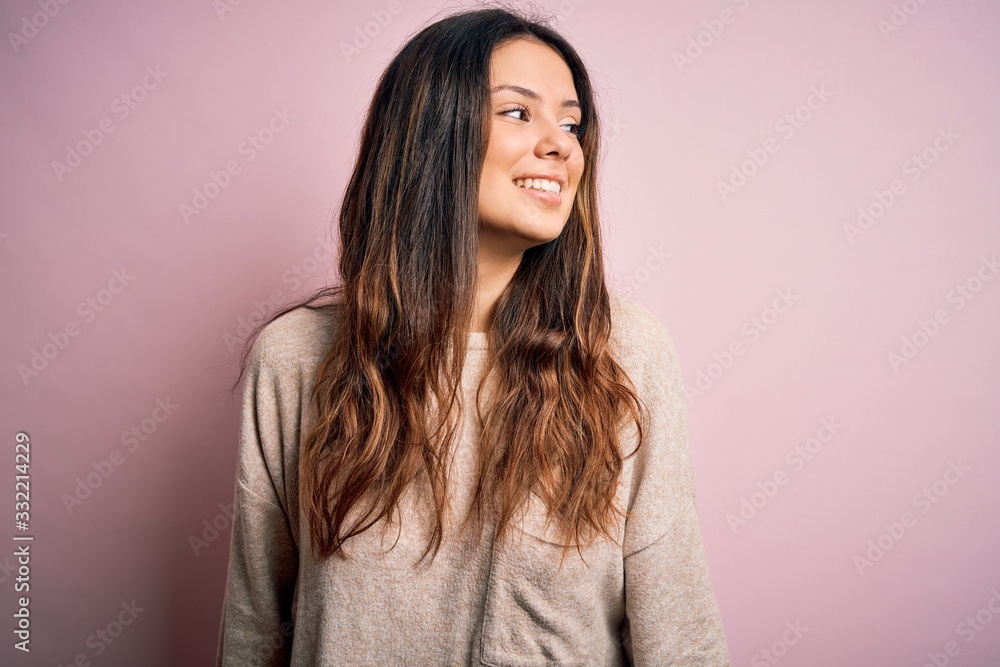 Young beautiful brunette woman wearing casual sweater standing over pink background looking away to side with smile on face, natural expression. Laughing confident. Young beautiful brunette woman wearing casual sweater standing over pink background looking away to side with smile on face, natural expression. Laughing confident.