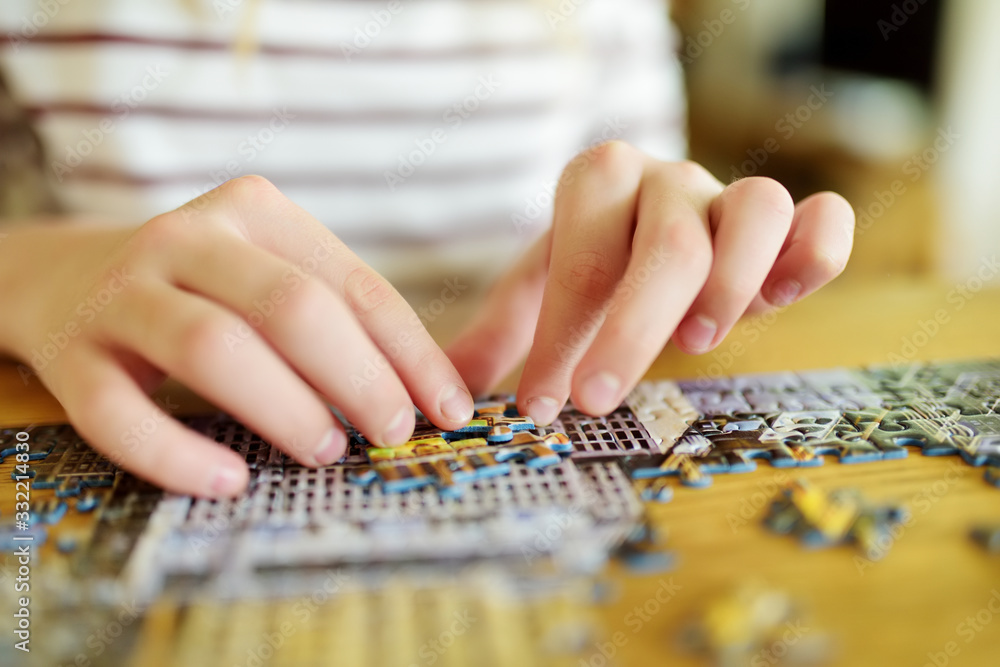 Fototapeta premium Close-up on child's hands playing puzzles at home. Child connecting jigsaw puzzle pieces in a living room table. Kid assembling a jigsaw puzzle. Stay at home activity for kids.