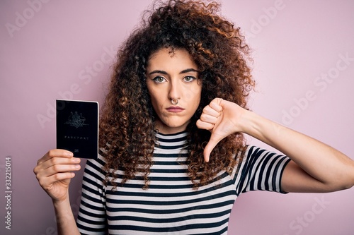 Beautiful tourist woman with curly hair and piercing holding australia australian passport id with angry face, negative sign showing dislike with thumbs down, rejection concept