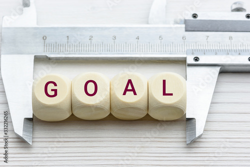 Measuring business goal setting / translate objectives into measurable goals concept : Vernier caliper and wood cubes with a word GOAL, depict tracking on progress or performance of a company targets photo