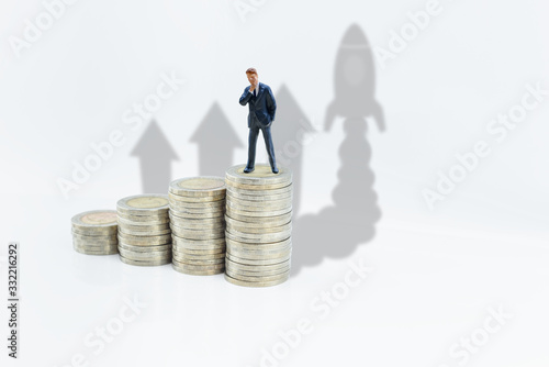 Business sales, corporate income or revenue and profit growth, financial concept : Miniature businessman on rows of increasing coins, thinks or makes long-term decision for sustainable earnings growth
