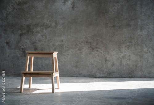 Empty wooden stepladder chair in the studio over concrete wall background with sunlight from one side