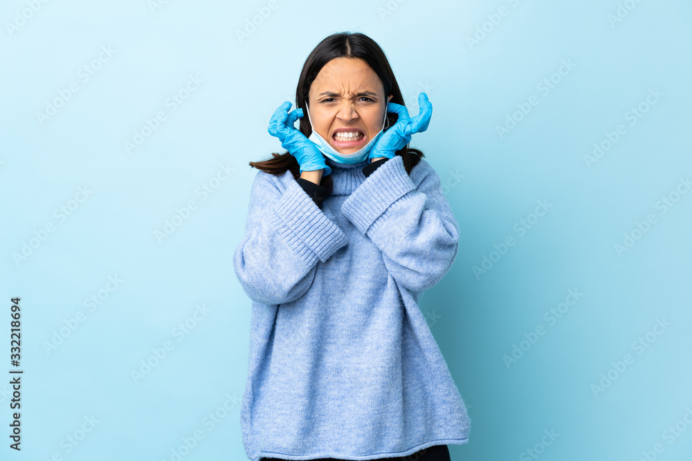 Young brunette mixed race woman protecting from the coronavirus with a mask and gloves over isolated blue background frustrated and covering ears Young brunette mixed race woman protecting from the coronavirus with a mask and gloves over isolated blue background frustrated and covering ears