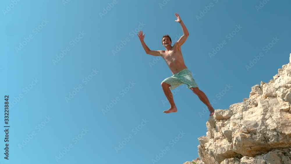 SLOW MOTION: Cinematic shot of a happy male tourist cliff diving in Croatia. Joyful man outstretches arms and legs as he jumps off a rocky ledge to dive into the refreshing sea on a sunny summer day. SLOW MOTION: Cinematic shot of a happy male tourist cliff diving in Croatia. Joyful man outstretches arms and legs as he jumps off a rocky ledge to dive into the refreshing sea on a sunny summer day.