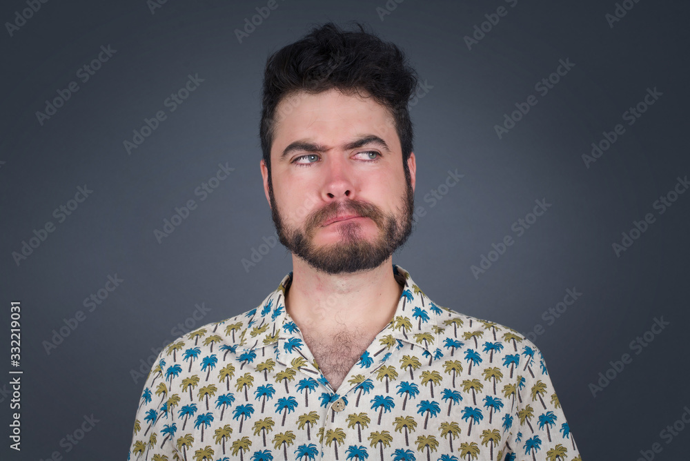 Photo of amazed puzzled young Caucasian male with ginger hair knot, curves lips and has worried look, sees something awful in front, isolated on white background, dressed in jean overalls. Photo of amazed puzzled young Caucasian male with ginger hair knot, curves lips and has worried look, sees something awful in front, isolated on white background, dressed in jean overalls.