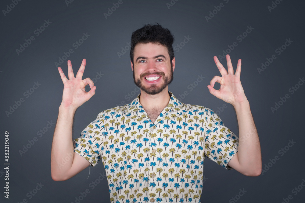 Glad attractive man shows ok sign with both hands as expresses approval, has cheerful expression. Photo of beautiful female has appealing appearance, being optimistic. Standing against gray wall. Glad attractive man shows ok sign with both hands as expresses approval, has cheerful expression. Photo of beautiful female has appealing appearance, being optimistic. Standing against gray wall.