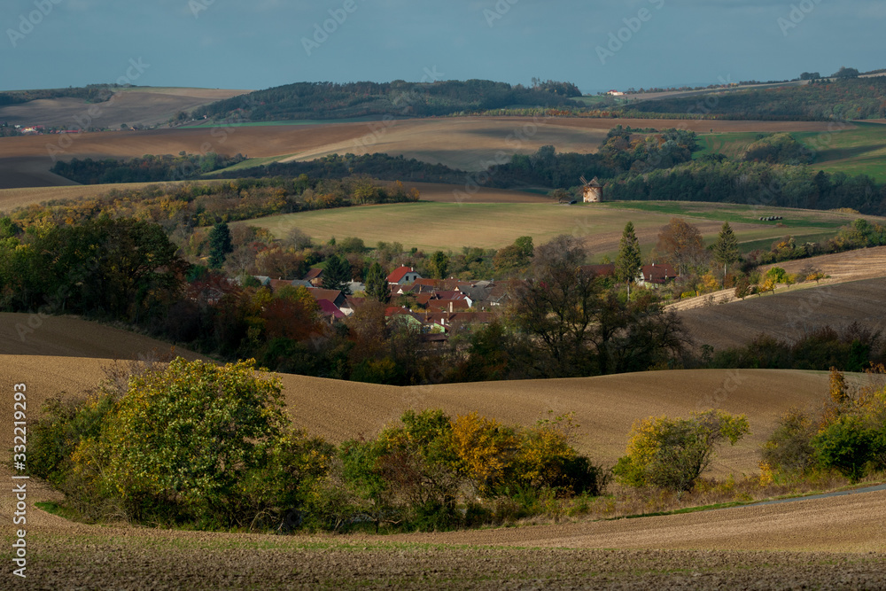 A Moravian village situated between arable fields, with a brick windmill in the background
