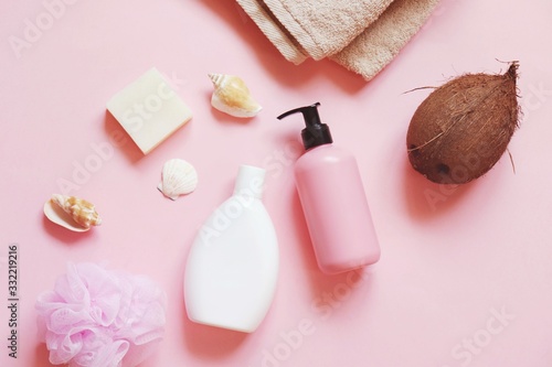 Spa cosmetics with natural organic ingredients. Bath products with coconut oil. White shampoo bottle, nourishing hair balm, beige cotton towel, soap bar and sponge on a pink background