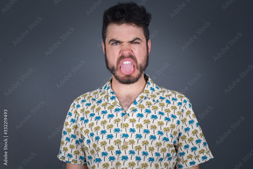 Fototapeta premium Body language. Disgusted stressed out pretty man posing against gray wall, frowning his face, demonstrating aversion to something.