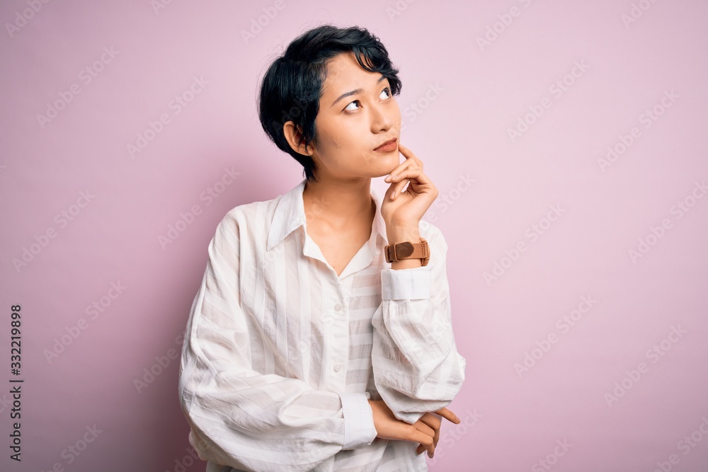 Young beautiful asian girl wearing casual shirt standing over isolated pink background with hand on chin thinking about question, pensive expression. Smiling with thoughtful face. Doubt concept. Young beautiful asian girl wearing casual shirt standing over isolated pink background with hand on chin thinking about question, pensive expression. Smiling with thoughtful face. Doubt concept.