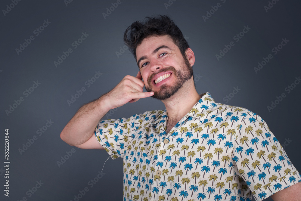 Fototapeta premium Attractive young male in casual clothes imitates telephone conversation, keeps hand near ear as if holding mobile phone, has confident facial expression, isolated outdoors. Call me!