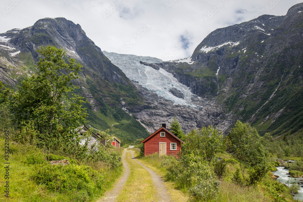 Abandoned village with different colored wooden houses in an idyllic location, between mountains, glacier in the background, abundant green vegetation on a summer day in Norway