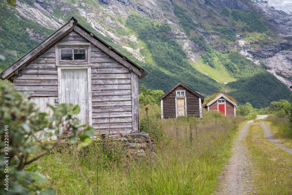 Fototapeta premium Abandoned village with different colored wooden houses in an idyllic location, between mountains, glacier in the background, abundant green vegetation on a summer day in Norway
