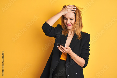 Obraz na plátně Young caucasian elegant business woman using smartphone over isolated yellow background stressed with hand on head, shocked with shame and surprise face, angry and frustrated