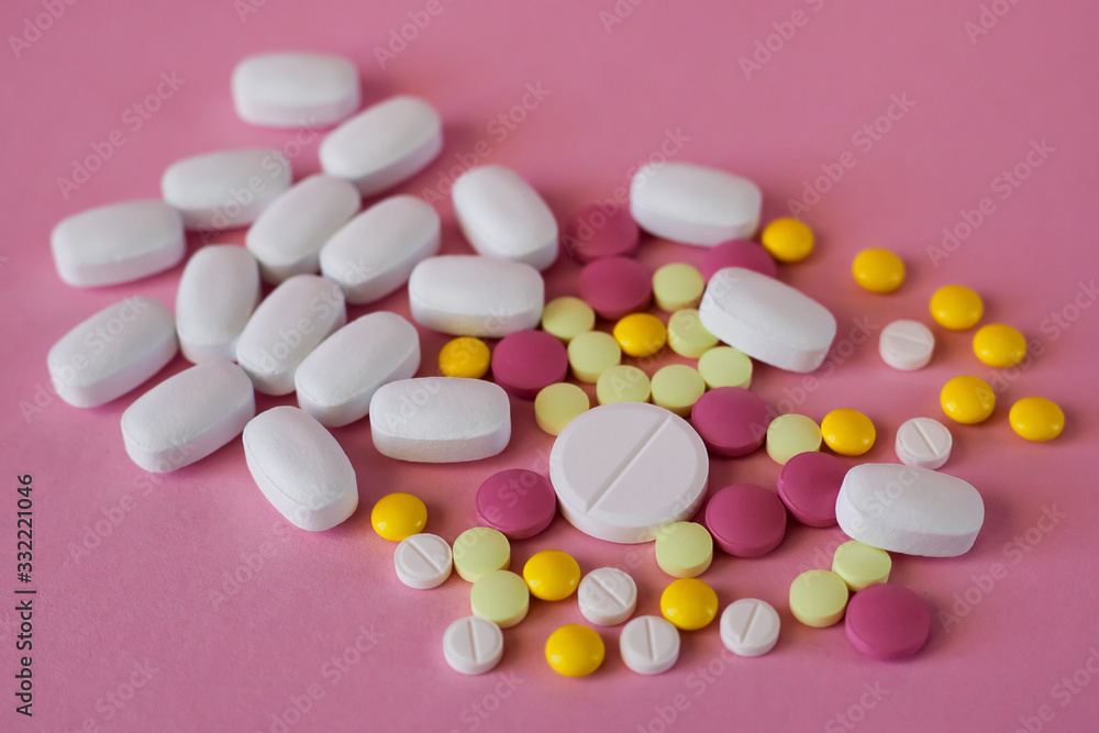 Assorted pharmaceutical medicine pills. Multi-colored pills of different shapes on a light pink background.