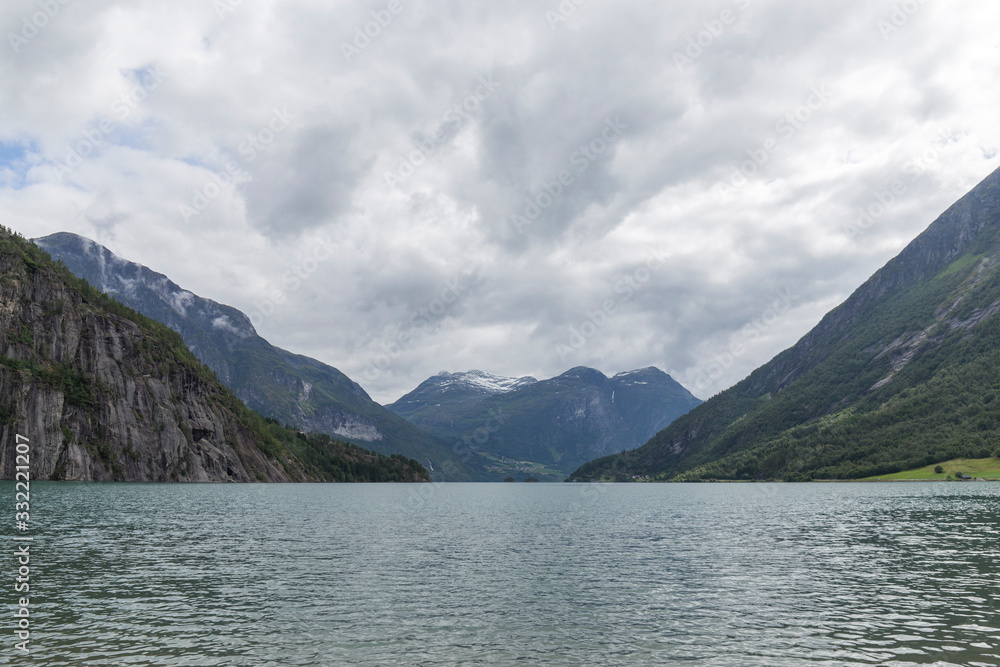 shore of a dark water fjord between mountains on a cloudy summer day in Norway