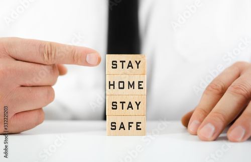 Businessman pointing to Stay Home, Stay Safe written on wooden blocks in a conceptual image for self quarantine times during virus outbreak.