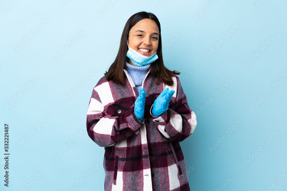 Young brunette mixed race woman protecting from the coronavirus with a mask and gloves over isolated blue background applauding after presentation in a conference Young brunette mixed race woman protecting from the coronavirus with a mask and gloves over isolated blue background applauding after presentation in a conference