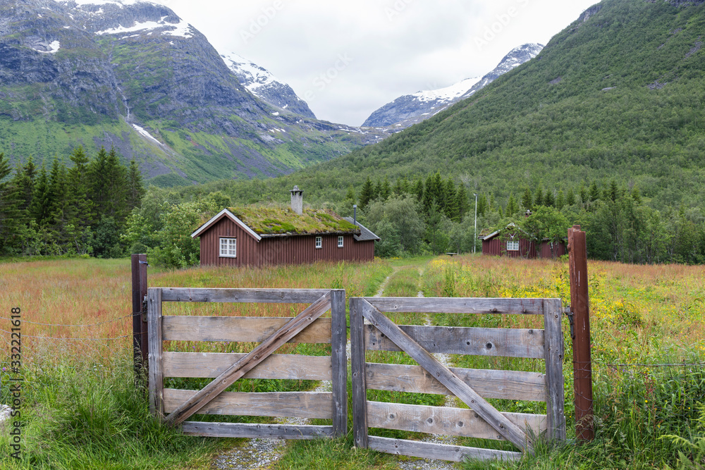 Abandoned village with different colored wooden houses in an idyllic location, between mountains, glacier in the background, abundant green vegetation on a summer day in Norway Abandoned village with different colored wooden houses in an idyllic location, between mountains, glacier in the background, abundant green vegetation on a summer day in Norway