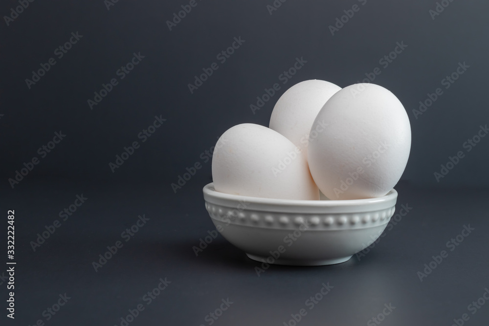 Eggs Sitting in white bowl isolated on studio black background three large eggs from grocery store. Eggs Sitting in white bowl isolated on studio black background three large eggs from grocery store.