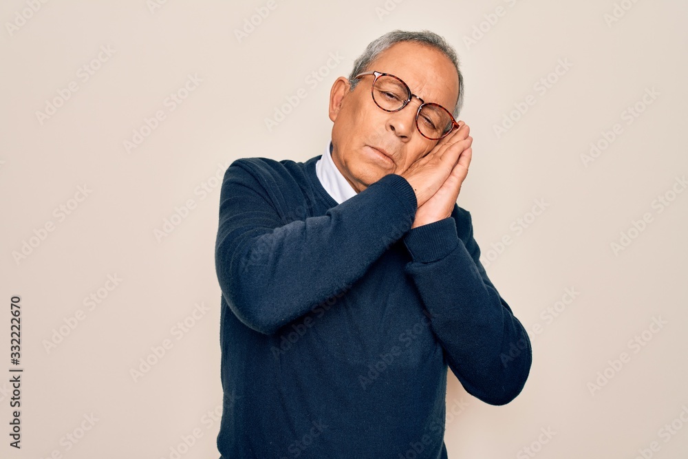 Senior handsome grey-haired man wearing sweater and glasses over isolated white background sleeping tired dreaming and posing with hands together while smiling with closed eyes. Senior handsome grey-haired man wearing sweater and glasses over isolated white background sleeping tired dreaming and posing with hands together while smiling with closed eyes.
