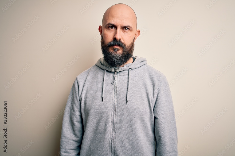 Fototapeta premium Handsome sporty bald man with beard wearing sweatshirt standing over pink background with serious expression on face. Simple and natural looking at the camera.