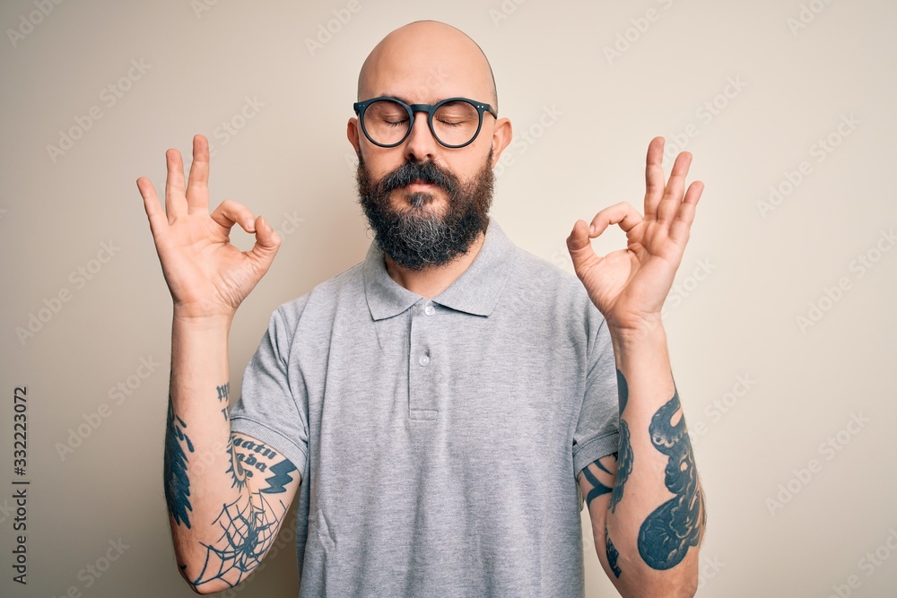 Naklejka premium Handsome bald man with beard and tattoo wearing casual polo and glasses relax and smiling with eyes closed doing meditation gesture with fingers. Yoga concept.