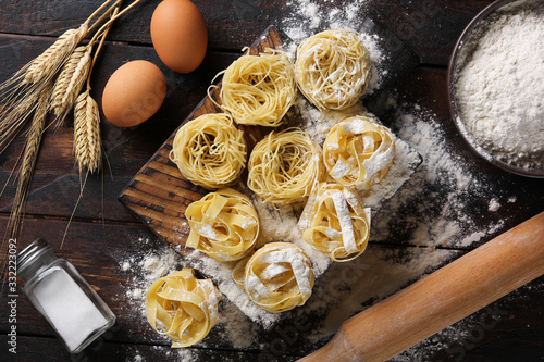 Concept of Italian cuisine. Dry pasta fettuccine and capellini with flour, eggs, rolling pin and salt. Wheat ears on an old wooden background. Background image photo