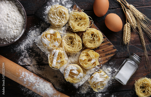 Concept of Italian cuisine. Dry pasta fettuccine and capellini with flour, eggs, rolling pin and salt. Wheat ears on an old wooden background. Background image photo