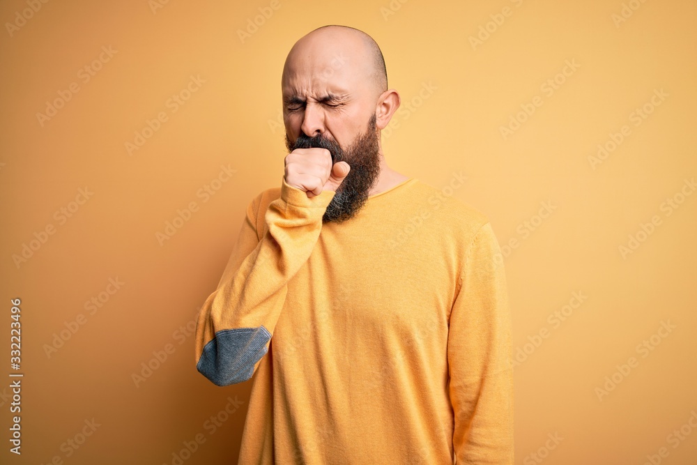 Handsome bald man with beard wearing casual sweater standing over yellow background feeling unwell and coughing as symptom for cold or bronchitis. Health care concept. Handsome bald man with beard wearing casual sweater standing over yellow background feeling unwell and coughing as symptom for cold or bronchitis. Health care concept.