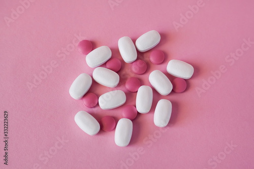 Large white oblong tablets and pink round tablets  on a light pink background. Antibiotics or drugs.