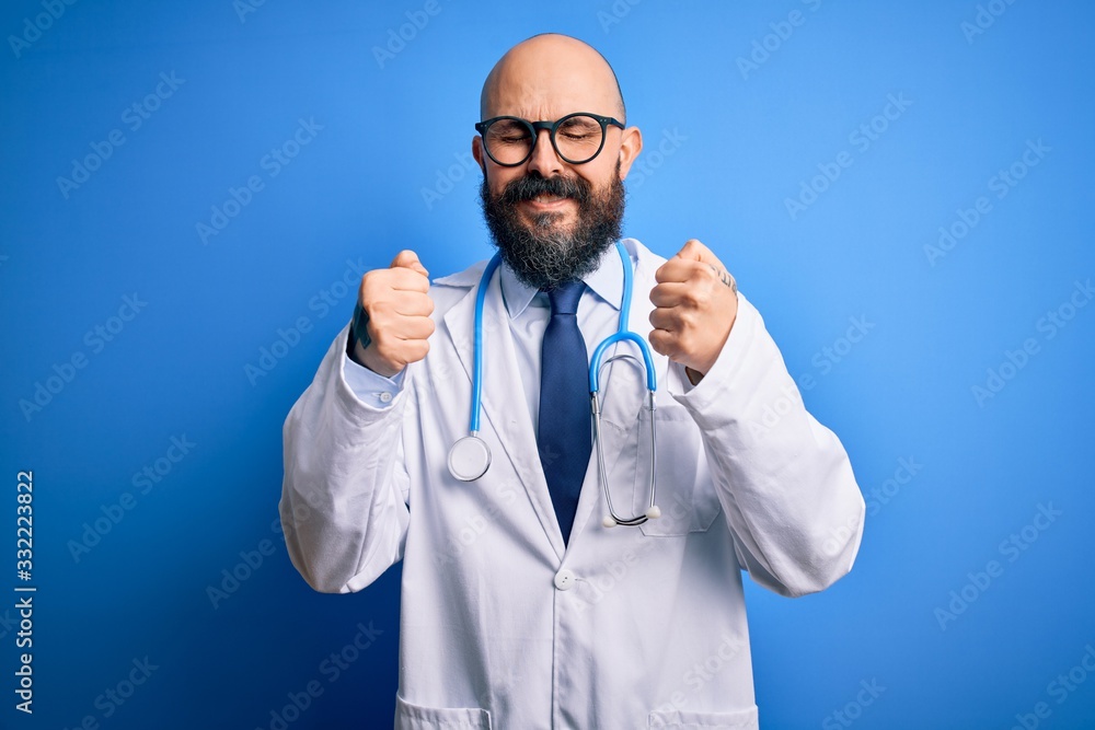 Handsome bald doctor man with beard wearing glasses and stethoscope over blue background excited for success with arms raised and eyes closed celebrating victory smiling. Winner concept. Handsome bald doctor man with beard wearing glasses and stethoscope over blue background excited for success with arms raised and eyes closed celebrating victory smiling. Winner concept.