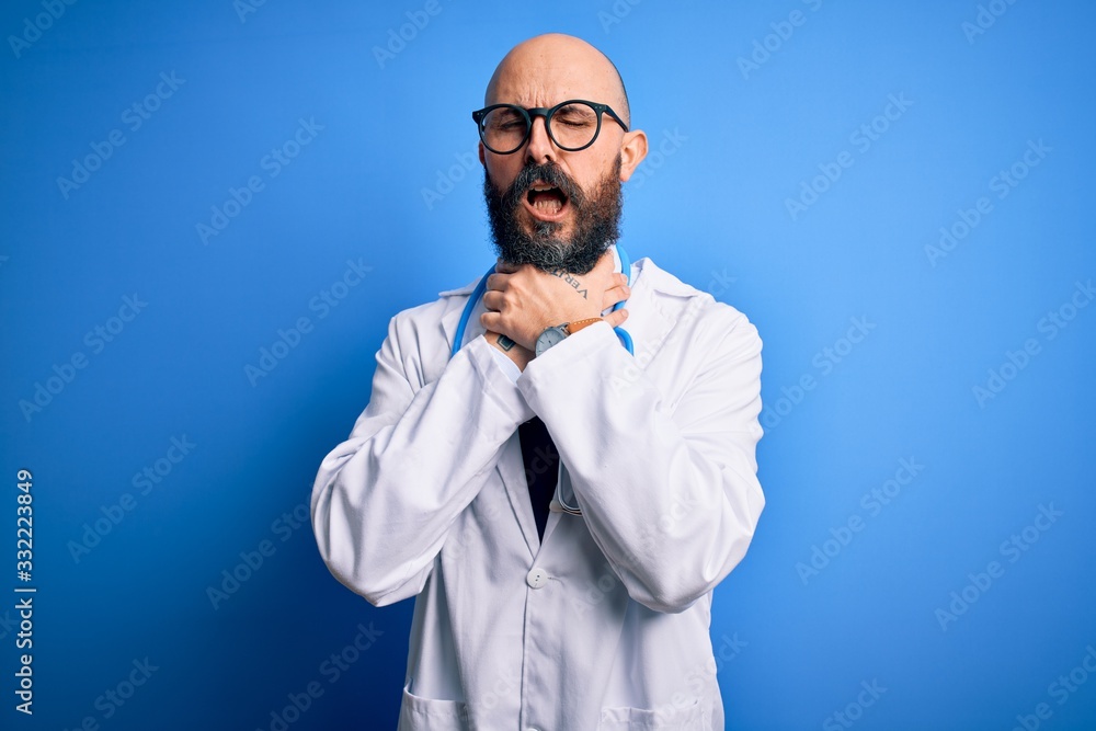 Handsome bald doctor man with beard wearing glasses and stethoscope over blue background shouting suffocate because painful strangle. Health problem. Asphyxiate and suicide concept. Handsome bald doctor man with beard wearing glasses and stethoscope over blue background shouting suffocate because painful strangle. Health problem. Asphyxiate and suicide concept.
