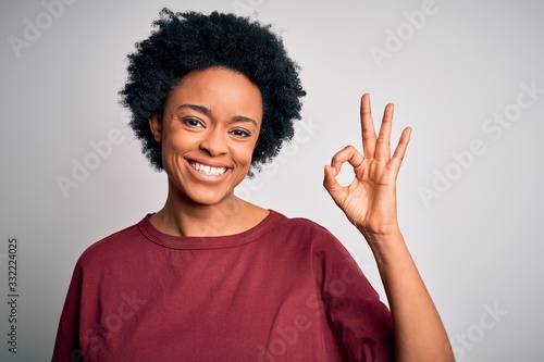 Young beautiful African American afro woman with curly hair wearing casual t-shirt standing smiling positive doing ok sign with hand and fingers. Successful expression.