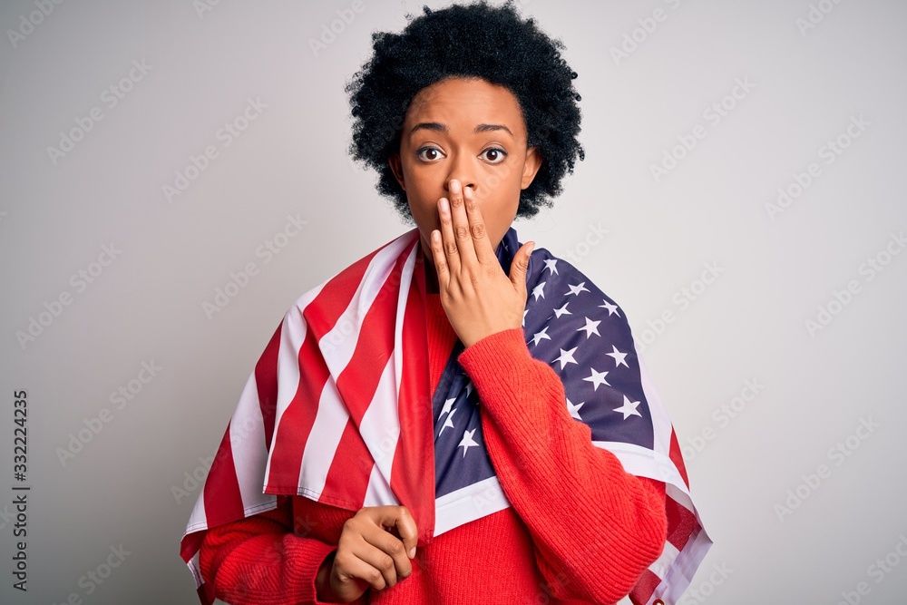Young African American afro woman with curly hair wearing united states of america flag cover mouth with hand shocked with shame for mistake, expression of fear, scared in silence, secret concept Young African American afro woman with curly hair wearing united states of america flag cover mouth with hand shocked with shame for mistake, expression of fear, scared in silence, secret concept