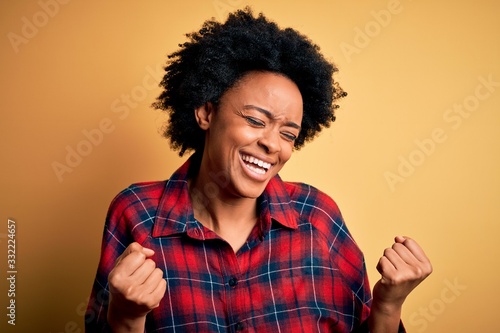 Young beautiful African American afro woman with curly hair wearing casual shirt very happy and excited doing winner gesture with arms raised, smiling and screaming for success. Celebration concept. © Krakenimages.com